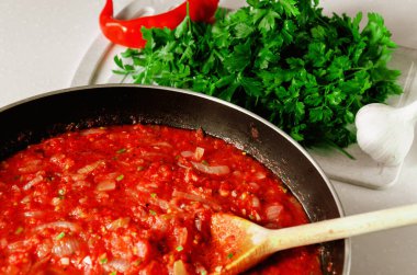 Marinara sosu. Makarna için ev yapımı domates sosu ya da tahta kaşıkla tavada spagetti. Taze yeşil maydanoz, biber ve sarımsak. Yakın çekim.