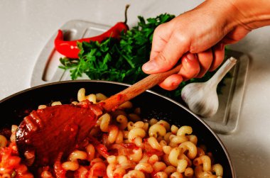 Marinara soslu geleneksel Akdeniz makarnası. Kadın makarnayla ev yapımı domates sosunu karıştırıyor. Yakın çekim.
