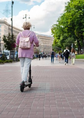Şehir caddesinde elektrikli scooter kullanan tanınmayan yetişkin bir kadın. Dikiz aynası. Dikey oryantasyon. Şehirde çevre dostu alternatif ulaşım kavramı
