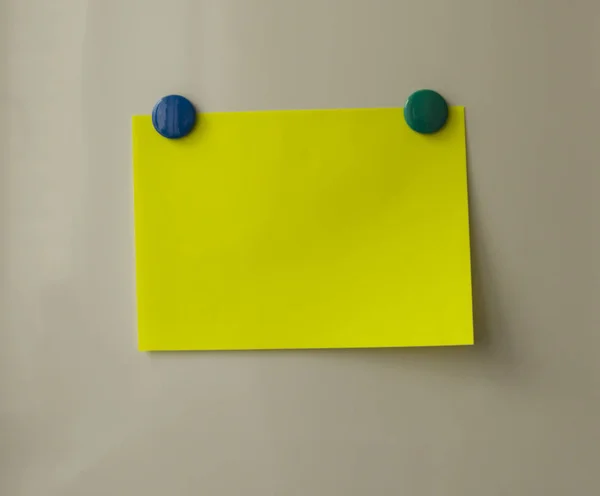 Yellow blank note on beige background, green and blue magnets