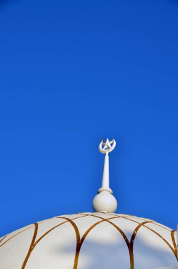 Mavi gökyüzünün arka planına karşı bir caminin tepesinde yer alan bir kuş