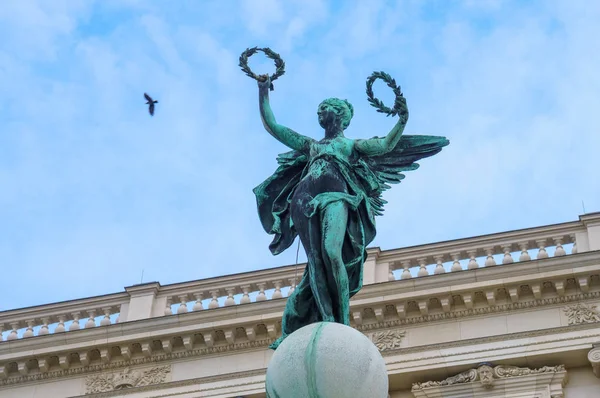 Estatua oxidada de piedra con dos guirnaldas en los brazos y con pájaro en el fondo del cielo claro en Viena — Foto de Stock