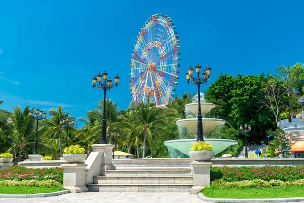 Tropikal ağaçlar ve merdivenler ile eğlence parkında dönme dolap ve çeşme