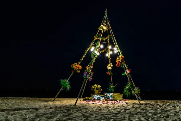 Sahilde kum üzerinde geceleri ampuller ve çiçekler ile ahşap kulübe