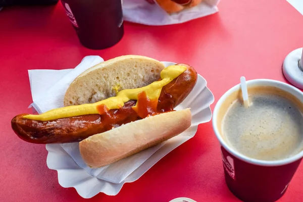 Fried sausage in a bun with mustard and ketchup with coffee in a cafe — Stock Photo, Image