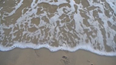Denizde köpüklü dalgalar kumda ayak izlerini yıkayın