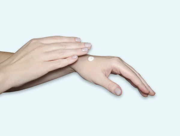 A woman\'s hands, a drop of white moisturizer on her arm. Hand care, skin hydration