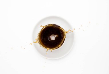 Bir küp şeker beyaz bir fincan kahveye düşer, su sıçratır. Üst görünüm, beyaz arkaplan.