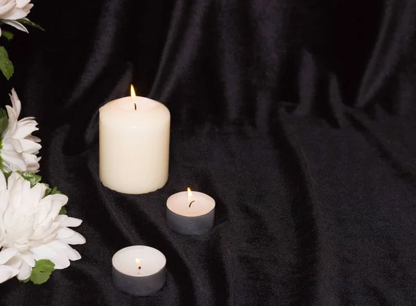 The concept of funeral service. Candles and white flowers on a black background. Free space for text.