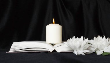 Başınız sağ olsun. Beyaz çiçekli beyaz bir anıt mum ve açık bir kitap. Cenaze, üzüntü..