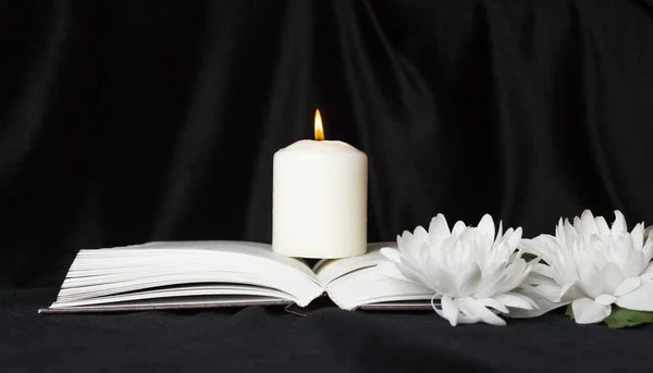 Condolence card. A white memorial candle with white flowers and an open book. The funeral, the sadness.