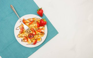 Modaya uygun yiyecekler. Krep gevreği. Beyaz arka planda turkuaz peçeteli mini mısır gevreği yığını. Çilek ve çatal. Metin için kalan boşluğu kopyala. Üst görünüm veya düz uzanma.
