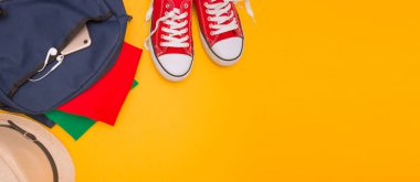 The concept of tourism, travel, minimalism. Red sneakers, backpack, phone and headphones on a yellow background. Yellow bright background, free space for text, top view. clipart