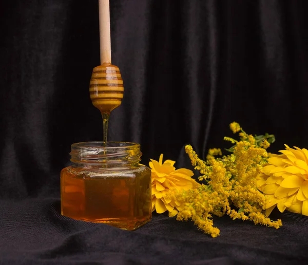 蜂の蜂蜜は木製のへらからガラス瓶に落ちる 黄色の花 黒の背景 便利な農産品 — ストック写真