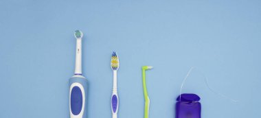 Ağız temizliği. Mavi arka planda elektrikli diş fırçası, diş fırçası ve diş ipi parçası. Yukarıdan görünüşü.