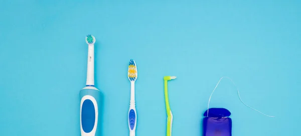 Oral hygiene. Part of an electric toothbrush, toothbrushes and floss on a blue background. The view from the top. — Stock Photo, Image