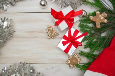 Açık ahşap arka planda kırmızı kurdeleli iki hediye kutusu, zencefil şekilli kurabiyeler ve Noel ağacı dalları. Yeni yıl ve Noel kavramı, hediyeler, tatil. Üst görünüm, kopyalama alanı.