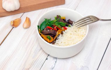 Biberli biftek ve beyaz pirinç. Beyaz tabak, arka planda sarımsak. Yan görüş. Lezzetli yemek.