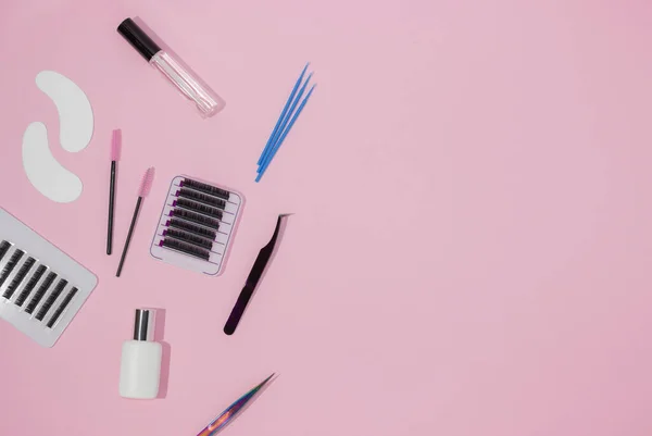 Tools for eyelash extensions on a pink background, free space for text, top view. Artificial eyelashes, tweezers, microbrushes, patches and brushes for lashmaker.