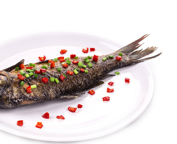 Close-up of a fried fish with spices. It is located in a white background.