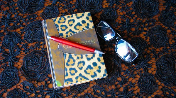 Dantel siyah masa örtüsü üzerinde kalem, defter ve gözlük.