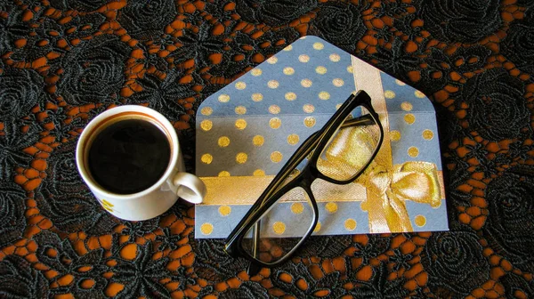 Siyah açık süs ile bir masa örtüsü üzerinde bir fincan kahve, bardak ve tebrik kartı.