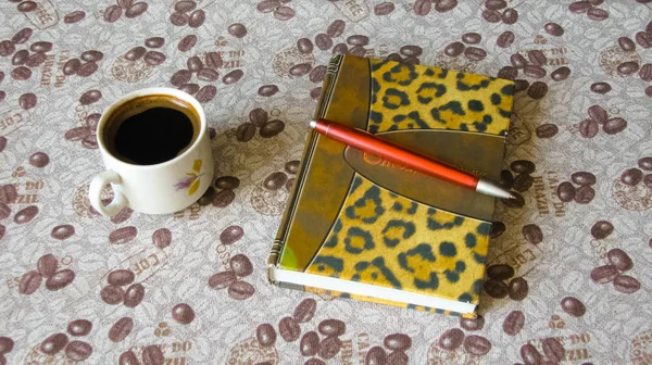 Kahve çekirdekleri ile masa örtüsü üzerinde kahve, defter ve kalem fincan.