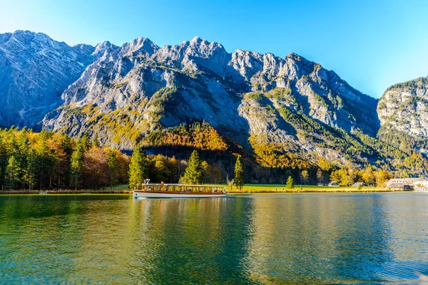 Sonbaharda Konigssee (Koenigssee, Koenigsee, Konigsee, Konigsee, Konig) gölünün manzarası, yakındaki St. Bartholomew Kilisesi (Bartholoma, Bartholomae) yakınlarında bir tekneyle. Berchtesgaden Ulusal Parkı, Bayern (Bavyera), Almanya
