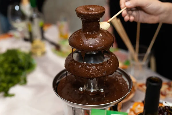 A chocolate fountain on party. Hand dipping banana slice into the fountain.