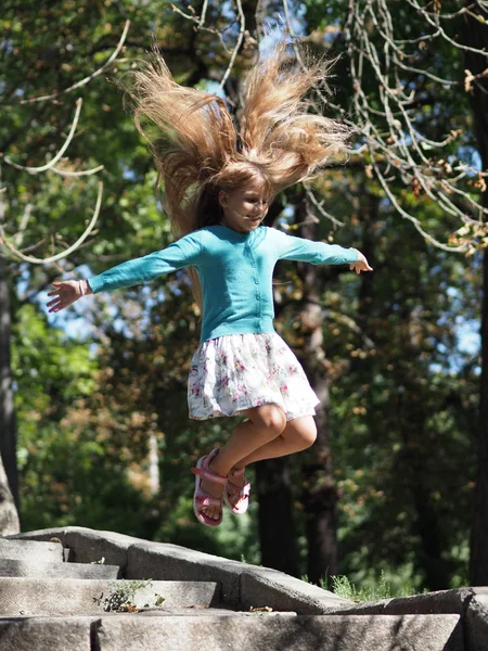 happy and cheerful girl on vacation in the park 9 years with long blond hair that develops during the jump