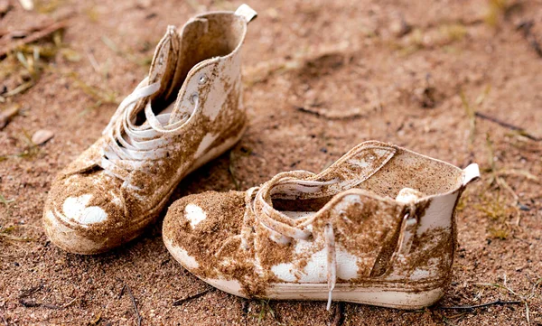 dirty lost white sneakers shoes lays in sand