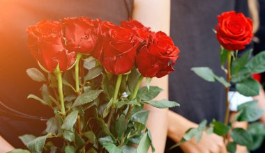 Kadının elinde büyük bir buket açık kırmızı gül..