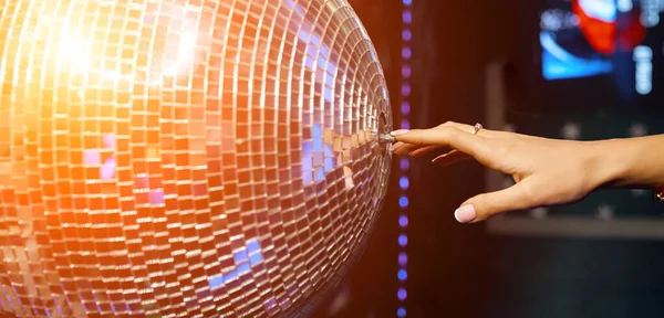 Beautiful female hand reaches for the disco ball and swings it