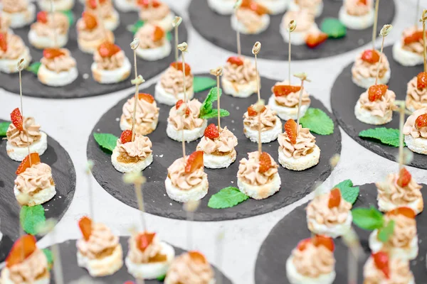 Lotes de canapés em bandejas pretas em uma mesa branca — Fotografia de Stock