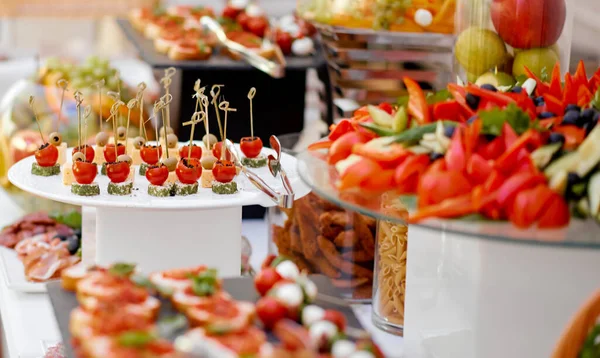 Catering. The table is richly richly filled with various snacks and vegetables. Focus on tomato and cheese snacks — Stock Photo, Image