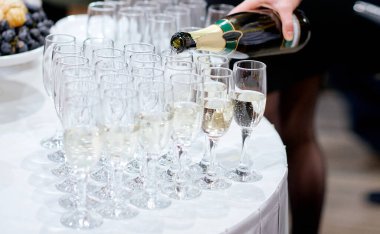 Garson beyaz masada ayarlanmış bardaklara şampanya doldurur.