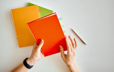 Kadın kırmızı bir defter seçti ve bunu ortaya çıkaracaktı. Arkasında turuncu ve yeşil defterler var..