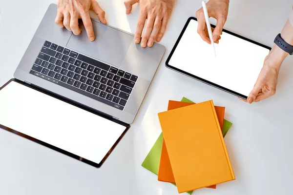 men work behind a laptop, a tablet with a stylus. Nearby lies a stack of colored notebooks