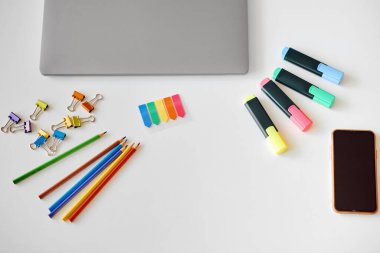 Masanın üzerinde çeşitli renkli kırtasiye dizüstü bilgisayar ve telefon var.