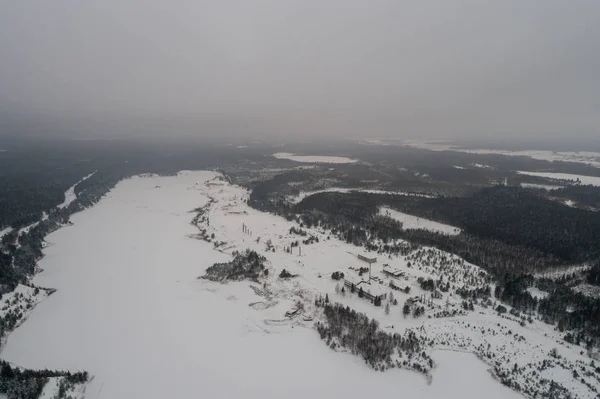 Aerial view of lake covered with snow. Forest.
