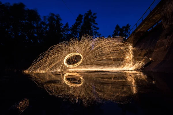 Burning steel wool spinned near the old dam. Showers of glowing sparks from spinning steel wool. Long exposure. Amazing reflections on water.