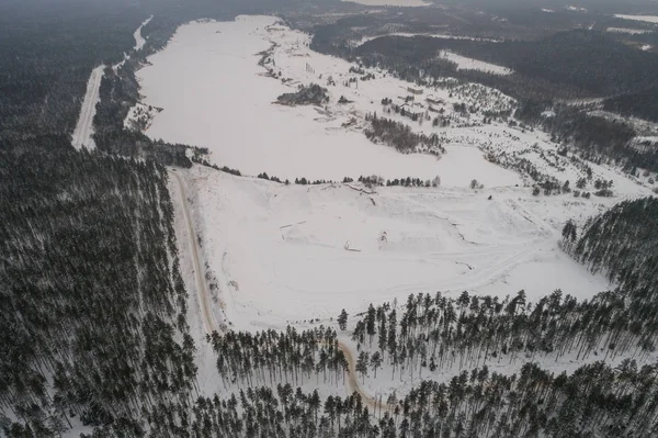 Aerial view of lake covered with snow. Forest.