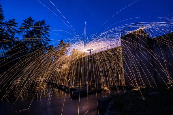 Burning steel wool spinned near the old dam. Showers of glowing sparks from spinning steel wool. Long exposure. Amazing reflections on water.