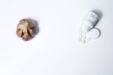 Fotoğraf beyaz bir arka plan üzerinde hap lar ile sarımsak gösterir.