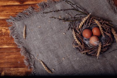 Boyalı Paskalya yumurtaları, kahverengi ahşap bir masada yer almakta ve doğal bir peçete ile kaplıdır.