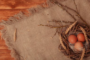 Boyalı Paskalya yumurtaları, kahverengi ahşap bir masada yer almakta ve doğal bir peçete ile kaplıdır.