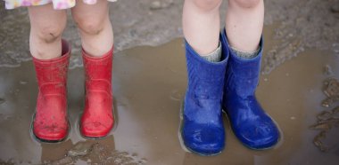 Lastik çizmeli çocuklar çamurlu bir su birikintisinde duruyorlar.