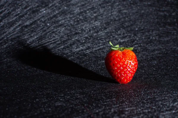 FIRST PLANE OF STRAWBERRY PROJECTING ITS SHADOW ISOLATED IN BACKGROUND WITH BLACK TEXTURES