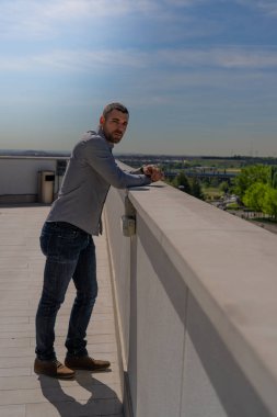 Genç yakışıklı bir adam kameraya bakar terasta ya da çatıda gülümserken mavi gökyüzüne