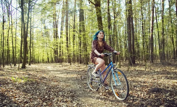 The girl in the dress rides a bicycle through the forest.